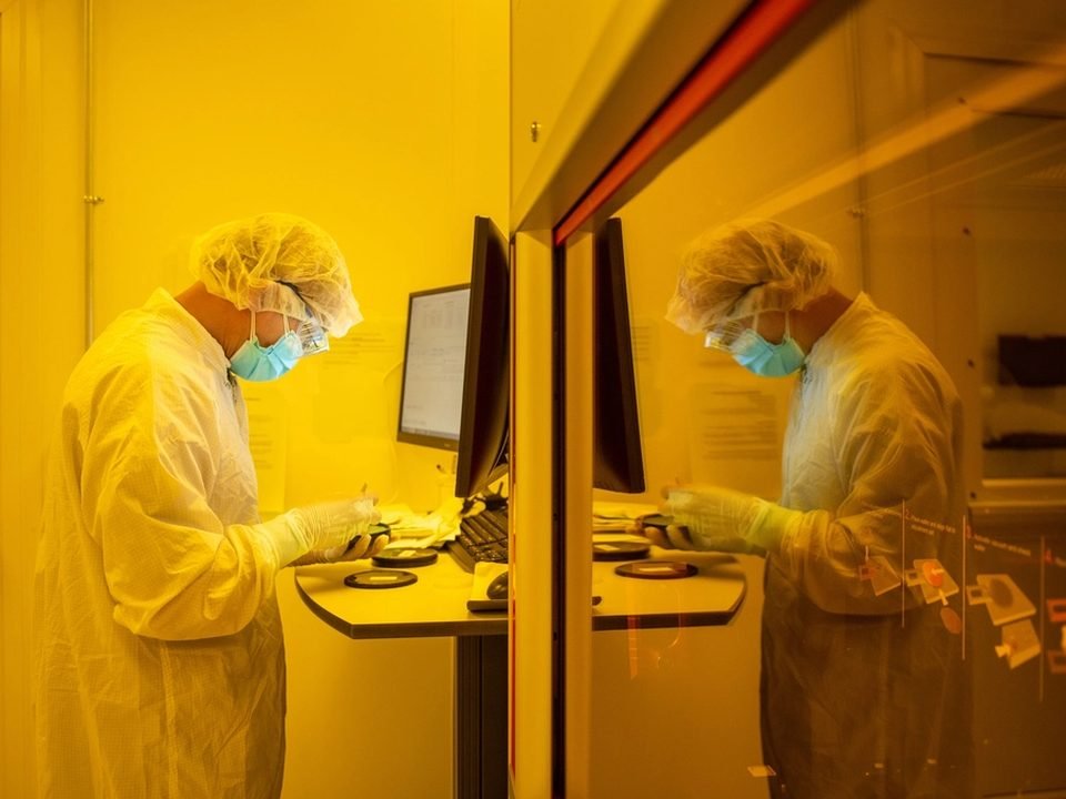 Engineer in a cleanroom suit working under lithography light